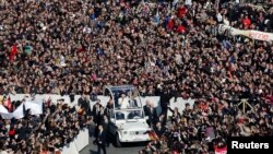 Paus Benediktus XVI, 85 tahun, melambaikan tangan kepada massa dari kendaraan terbuka yang bergerak perlahan melewati lapangan Santo Petrus untuk terakhir kalinya (27/2). 