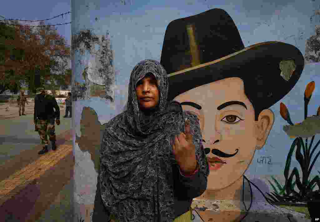 A woman shows her finger after voting in front of the painting of Bhagat Singh, an Indian revolutionary freedom fighter, during the first phase of Uttar Pradesh state elections in a village near Modinagar, India.
