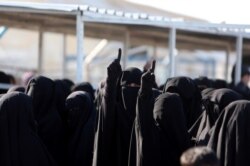 FILE - Women gesture as they stand together at the al-Hol displacement camp in Hasaka governorate, Syria, April 2, 2019.