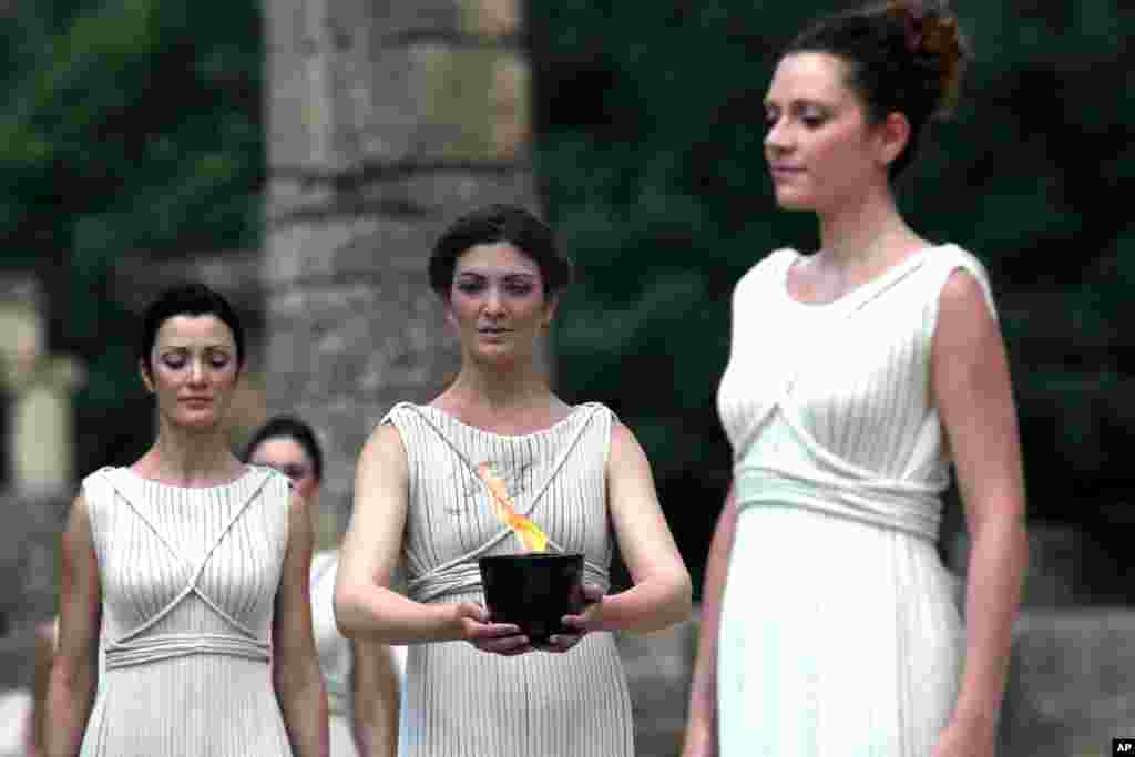 An actress portraying a priestess, right, holds a pot with the Olympic flame during the lighting of the flame ceremony at the site of ancient Olympia, Greece, May 10, 2012.