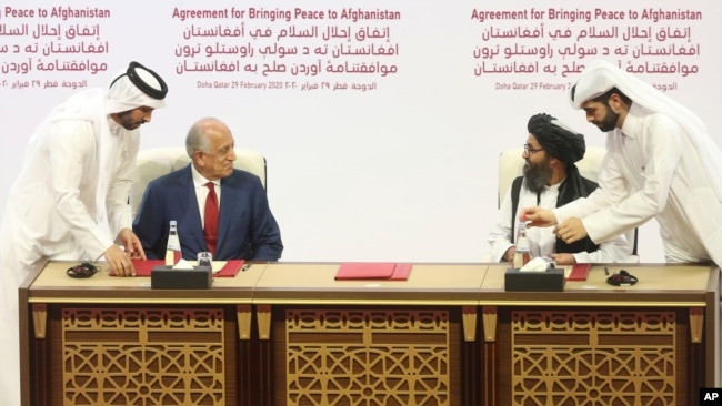 FILE - In this Feb. 29, 2020, photo, U.S. peace envoy Zalmay Khalilzad, left, and Mullah Abdul Ghani Baradar, the Taliban's top political leader, sign a peace agreement between Taliban and U.S. officials in Doha, Qatar.