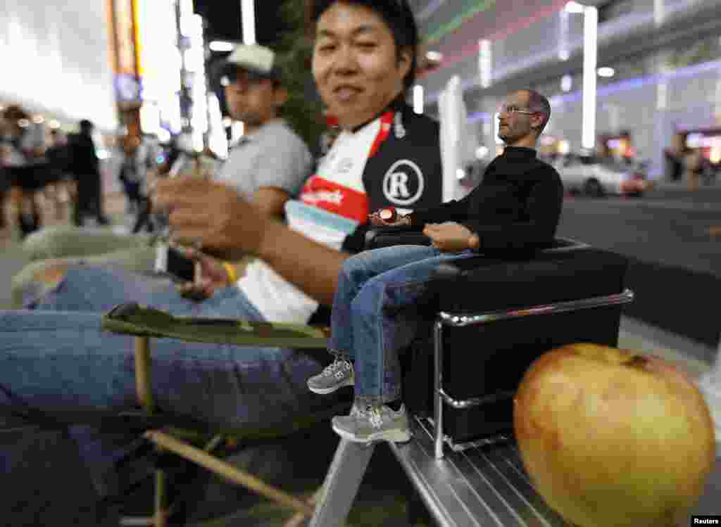 People sit next to a figurine of Apple's co-founder Steve Jobs and an apple as they wait for the release of Apple's new iPhone 5S near the Apple Store at Tokyo's Ginza shopping district, Japan.