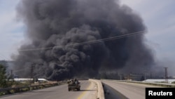 Smoke rises while members of the Syrian forces ride on a vehicle as they battle against a nascent insurgency by fighters from ousted leader Bashar al-Assad's Alawite sect, in Latakia, Syria March 7, 2025. 