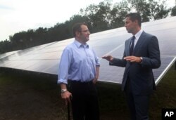 Michael Maravelias, left, an NRG Home Solar customer, and Kelcy Pegler Jr., president of NRG Home Solar, right, talk in front of solar panels from the NRG shared solar facility in Freetown, Massachusetts, July 27, 2015.