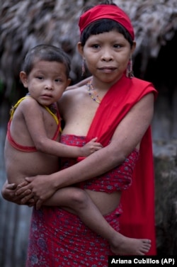 In this photo taken Sept. 7, 2012, a Yanomami Indian holds her son a their village called Irotatheri in Venezuela's Amazon region.