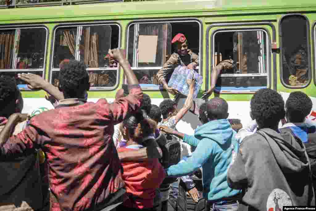 A soldier receives a pack of bottled water as people react while soldiers from the Ethiopian National Defence Forces drive through Sendafa.