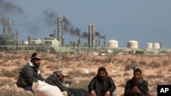 Anti-Gaddafi rebels sit on the ground near an oil facility in Ras Lanuf, March 10, 2011. The rebel leadership said on Thursday that the oil port of Ras Lanuf in eastern Libya is under heavy bombardment.