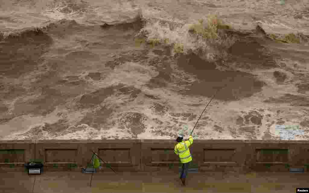 Seorang nelayan melemparkan kail ke laut dari tepi jalur pejalan kaki di Blackpool, Inggris.