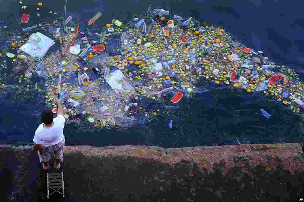A man holds a fishing rod as floating trash hits the coastline of the Mediterranean Sea in Beirut, Lebanon.