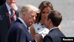 FILE - French President Emmanuel Macron shakes hands with U.S. President Donald Trump as first lady Melania Trump looks on after the traditional Bastille Day military parade in Paris, July 14, 2017. 