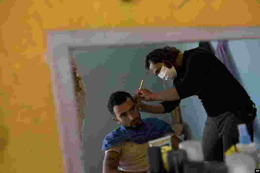 Seorang tukang cukur memangkas rambut seorang migran di kamp pengungsi Ritsona, utara Athena, Yunani.