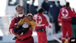 Red Cross volunteer Stavros Zembillis carries a little child just disembarked from a crippled freighter carrying hundreds of refugees trying to migrate to Europe, at the coastal Cretan port of Ierapetra, Greece, Nov. 27, 2014. 