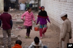 Two young girls carry a bucket to fetch water from a public tap at a slum in New Delhi, India, Dec. 29, 2015.