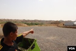 Faisel, 13, points at his house on the other side of the barbed-wire fence surrounding the camp, May 29, 2018, in Hassan Sham, Iraqi Kurdistan. (H. Murdock/VOA)