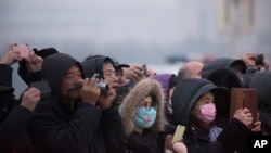 People wearing face masks walk take photos of the daily flag-lowering ceremony at Tiananmen Square on a day with poor air quality in Beijing, Nov. 28, 2015. 
