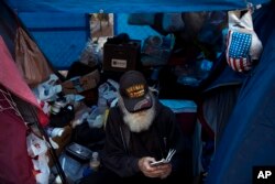 Theodore Neubauer, a 78-year-old Vietnam War veteran, who is homeless, looks at his smartphone while passing time in his tent, Dec. 1, 2017, in Los Angeles. "Well, there's a million-dollar view," said Neubauer on what it's like to be homeless in Los Angeles.