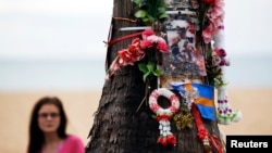 Женщина смотрит на дерево, декорированное цветами и фотографиями в память жертв цунами 2004 года. Таиланд. 26 декабря 2014 г.