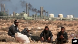 FILE - Anti-Gadhafi rebels sit on the ground near an oil facility in Ras Lanuf, Libya. The struggle for the Ras Lanuf refinery and nearby Sidr depot threatens to spiral into an all-out conflict between east and west.