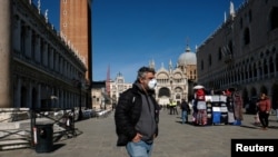 A man wearing a protective mask walks through an empty Saint Mark's Square in Venice as Italy battles a coronavirus outbreak, Venice, Feb. 27, 2020.