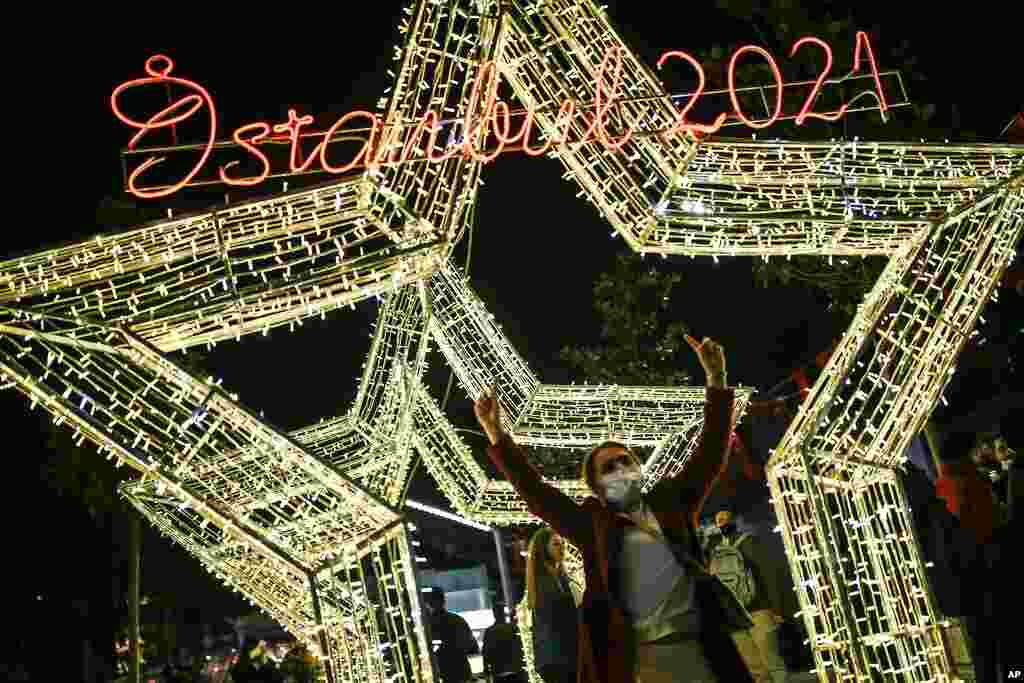 A woman, wearing a mask to help protect from the spread of the coronavirus, poses for photographs in front of decorations in central Istanbul&#39;s Taksim Square, Dec. 31, 2020. 