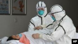 Personal sanitario provisto con trajes protectores traslada a una paciente infectada con coronavirus a un pabellón de aislamiento en el Segundo Hospital del Pueblo en Fuyang, provincia de Anhui, en el centro de China. (Chinatopix vía AP)