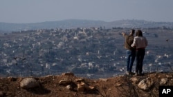 An Israeli couple observe the damaged buildings of a village in southern Lebanon as they stand near the Israeli-Lebanese border, during the ceasefire between Israel and Hezbollah, on Nov. 30, 2024.