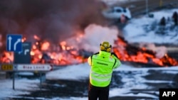 A road agency worker takes a picture as molten lava flows over the road leading to the tourist destination Blue Lagoon spa near Grindavik, Iceland, on Feb. 8, 2023.