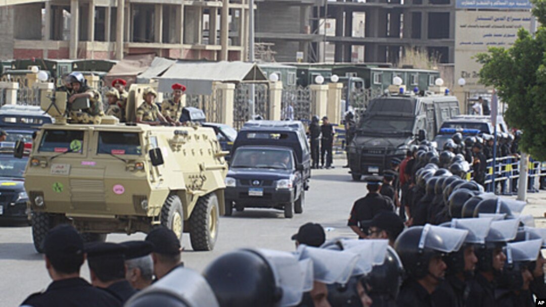 Egyptian policemen line the street as an armored army vehicle guards a convoy carrying former Egyptian interior minister Habib el-Adly and his aides, as they arrive at the court in Cairo, May 21, 2011