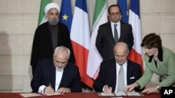 Presiden Iran Hassan Rouhani dan Presiden Perancis Francois Hollande menyaksikan kesepakatan bilateral antara Iran-Perancis yang ditandatangai Menlu Javad Zarif (kiri) dan Laurent Fabius di Paris (foto: dok). Bank-bank internasional masih enggan mendanai kesepakatan bisnis dengan Iran pasca dicabutnya sanksi ekonomi.