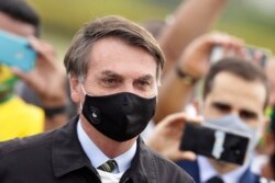 Brazilian President Jair Bolsonaro, wearing a face mask amid the new coronavirus pandemic, stands amid supporters taking pictures with cell phones as he leaves his official residence of Alvorada palace in Brasilia, Brazil, May 25, 2020.