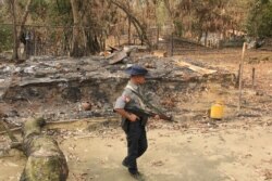 FILE - A Myanmar security officer walks past burned Rohingya houses in Ka Nyin Tan village of suburb Maungdaw, northern Rakhine state of western Myanmar, Sept. 6, 2017.