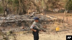 FILE - A Myanmar security officer walks past burned Rohingya houses in Ka Nyin Tan village of suburb Maungdaw, northern Rakhine state of western Myanmar, Sept. 6, 2017.