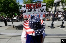 Cathy Camper, of Tacoma, Wash., wears a stars-and-stripes cowboy hat as she protests against Islamic law at a rally, June 10, 2017, in Seattle, as counter-protesters demonstrate across the street.