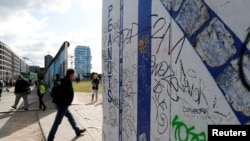 A pedestrian walks past segments of the East Side Gallery, the largest remaining part of the former Berlin Wall, in Berlin, Germany, Sept. 19, 2019. 