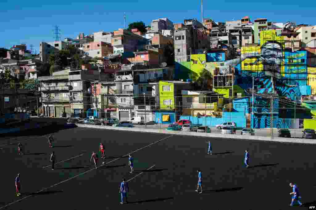 Residents play football in a field with the image of Brazilian football player Gabriel Jesus in the background, painted on the walls of houses in the Perus neighborhood, where he lived during his childhood in the outskirts of Sao Paulo, Brazil.