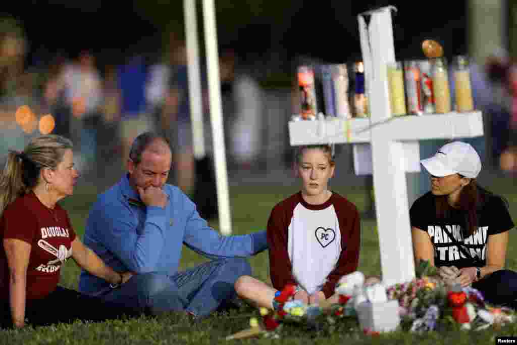 A family sits around one of 17 crosses at a memorial for the victims of the shooting at Marjory Stoneman Douglas High School in Parkland, Florida, Feb. 16, 2018.