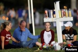 A family sits around one of 17 crosses at a memorial for the victims of the shooting at Marjory Stoneman Douglas High School in Parkland, Florida, Feb. 16, 2018.
