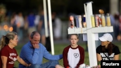 Una familia se sienta alrededor de una de las 17 cruces en un monumento a las víctimas del tiroteo en Marjory Stoneman Douglas High School en Parkland, Florida, el 16 de febrero de 2018.
