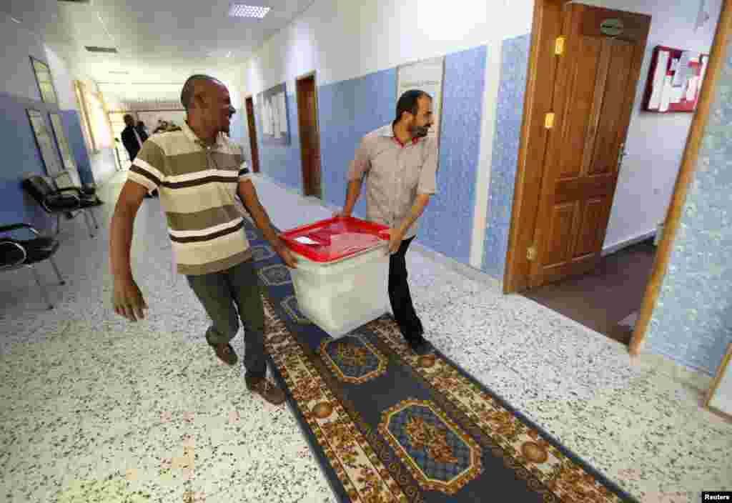 Para petugas pemilu mengangkat kotak suara ke sebuah sekolah menjelang pelaksanaan pemilu di Tripoli (24/6). 