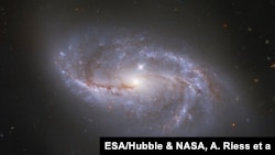 Con una visión profunda hacia el Universo, el Telescopio Espacial Hubble de NASA/ESA vislumbra las numerosas estructuras en forma de brazos que se mueven alrededor de esta galaxia espiral barrada, conocida como NGC 2608.