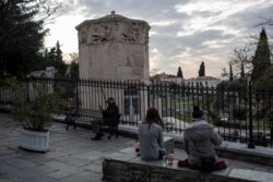 Visitantes sentados frente a la Torre de los Vientos en la antigua Ágora (mercado) romana en Atenas, el 9 de marzo de 2021. Grecia registra un alto récord diario de infecciones de covid para este año y de los más altos en lo que va de la pandemia.