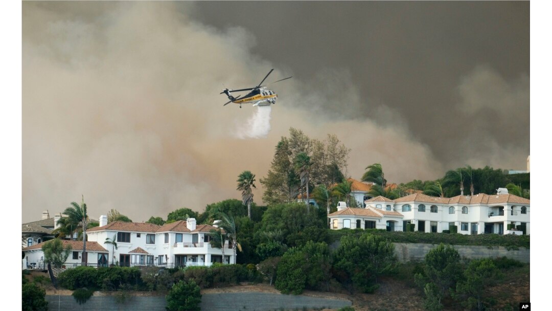 A helicopter drops water on a brush fire behind homes during the Woolsey Fire in Malibu, Calif., Nov. 9, 2018. A fast-moving wildfire in Southern California has scorched a historic movie site and forced numerous celebrities to join the thousands fleeing from the flames.