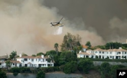 A helicopter drops water on a brush fire behind homes during the Woolsey Fire in Malibu, Calif., Nov. 9, 2018.