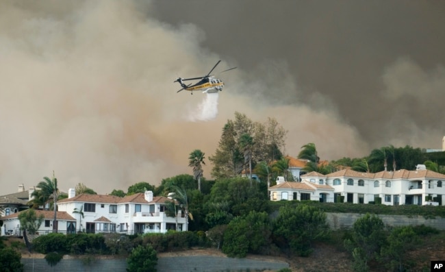 A helicopter drops water on a brush fire behind homes during the Woolsey Fire in Malibu, Calif., Nov. 9, 2018. A fast-moving wildfire in Southern California has scorched a historic movie site and forced numerous celebrities to join the thousands fleeing from the flames.