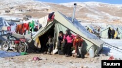 FILE - Syrian refugees sit by their tent in a Syrian refugee camp on the Lebanese border town of Arsal, in the eastern Bekaa on December 15, 2013. 