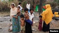 FILE - A family stands beside remains of a market which was set on fire, in Rohingya village outside Maungdaw, in Rakhine state, Myanmar. 