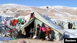 FILE- Syrian refugees sit by their tent in a Syrian Refugee camp on the Lebanese border town of Arsal, in the eastern Bekaa, Dec. 15, 2013.