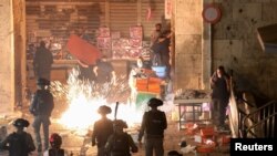 Palestinians react as Israeli police fire a stun grenade during clashes at Damascus Gate on Laylat al-Qadr during the holy month of Ramadan, in Jerusalem's Old City, May 9, 2021. 