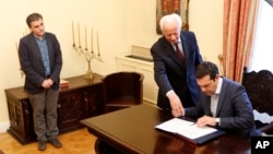 Greece's Prime Minister Alexis Tsipras, right, signs a protocol as the new Greek Finance Minister Euclid Tsakalotos, left, looks on during the swearing in ceremony at Presidential Palace in Athens, Monday, July 6, 2015.