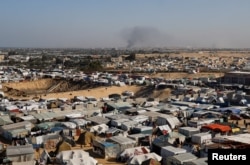 Sebuah kamp tenda yang menampung warga Palestina yang terlantar, ketika asap mengepul di kejauhan akibat operasi darat Israel di Khan Younis, 22 Januari 2024. (Foto: REUTERS/Ibraheem Abu Mustafa)